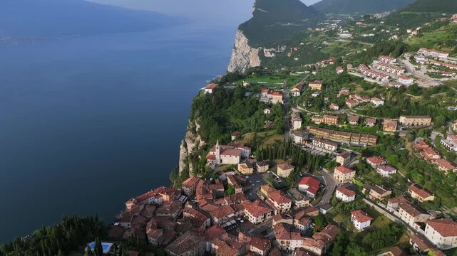 High altitude, cinematic 4k drone shot of Tremosine Pieve, a quaint and picturesque Italian village with red roof tiles high above the dramatic sheer cliffs of Lake Garda in Summer