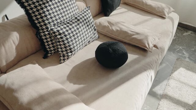 Sunlight streams into a modern living room, illuminating a beige sofa adorned with patterned and textured cushions. A sense of calm and comfort pervades the minimalist space.