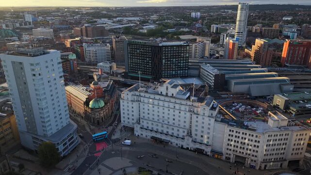 Aerial video overlooking Leeds city centre streets and architecture towards the railway station and skyline under morning Sun.