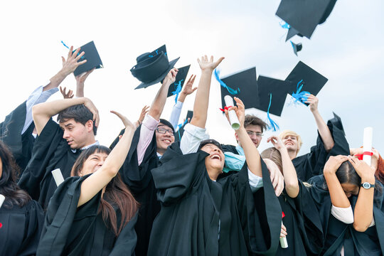 Graduates in caps and gowns joyfully toss hats in celebration.
