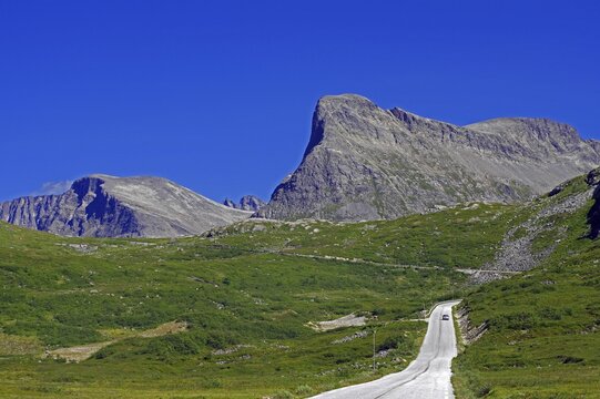 A clear road leads through a green mountain landscape under a blue sky, Trollstigen, Andalsnes, Norway