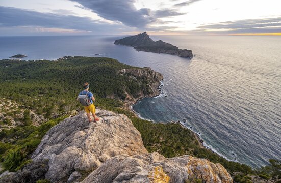 View of mountains and coast with sea, at sunset, hikers on a rock, hiking to La Trapa from Sant Elm, back island Sa Dragonera, Serra de Tramuntana, Majorca, Spain