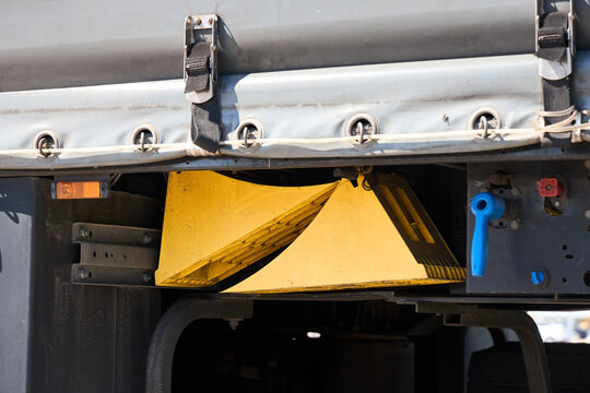 Yellow wheel chocks stored under heavy truck trailer frame, ensuring safety, stability, transport security, and vehicle prevention from rolling during parking or maintenance operations.