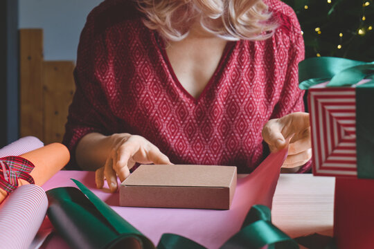 Woman carefully wrapping a gift with paper and ribbon at home.
The scene illustrates gift preparation, personalized shopping, product presentation and consumer gifting for special occasions.