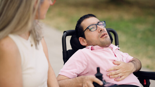 Man with spina bifida sitting in a power wheelchair and talking with his caregiver outdoors, symbolizing support and care
