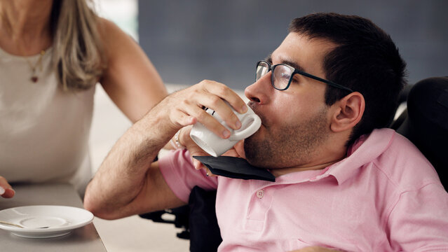 Young man with spina bifida and physical disability drinking coffee in a cafe, showing inclusion and accessibility
