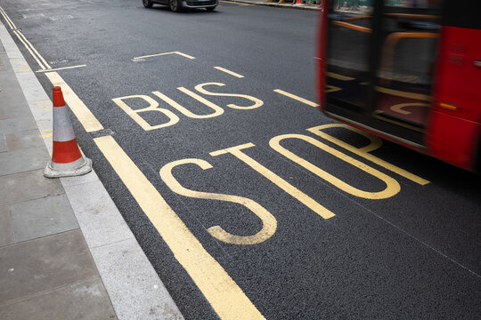 Red bus passing bus stop road markings in the city.
