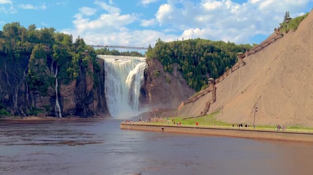 Wide scenic view of Montmorency Falls with tourists exploring the park grounds in Quebec City, Quebec, Canada.