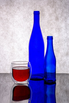 Still life with blue glass bottles and a glass of wine on a gray background