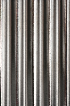 Full frame background texture of a metallic crinkle cutter blade with shiny vertical wavy lines.