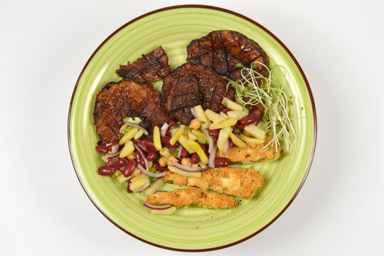 Three grilled celeriac steaks served with breaded celery stalks mixed bean salad and fresh sprouts on a light green ceramic plate.