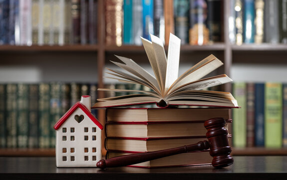 A judge's gavel and a symbolic house set against a backdrop of bookshelves.