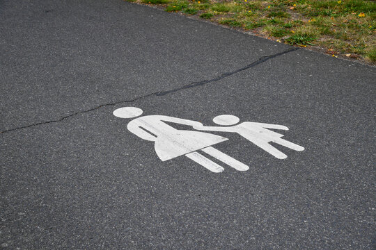 Wei&szlig;e Bodenmarkierung f&uuml;r Fu&szlig;g&auml;nger mit erwachsener Person und Kind auf Asphalt. Familienweg, Fu&szlig;weg, Sicherheit, Orientierung, &ouml;ffentlicher Raum und sichere Wegef&uuml;hrung.