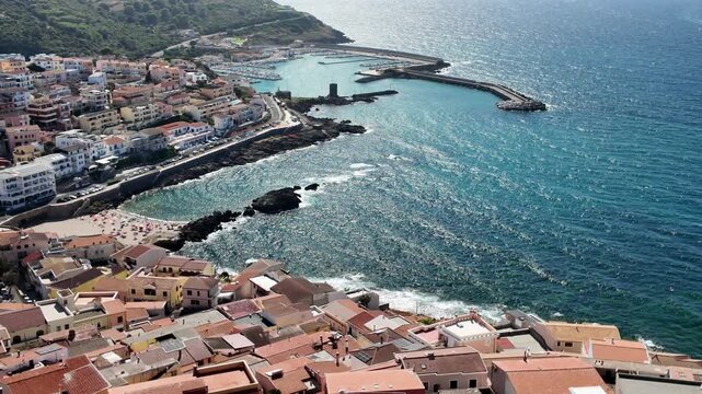 Picturesque elevated view of the seaside town of Castelsardo in Sardinia, Italy, featuring its characteristic dense cluster of buildings with orange roofs, a sandy beach in the cove, and a harbor
