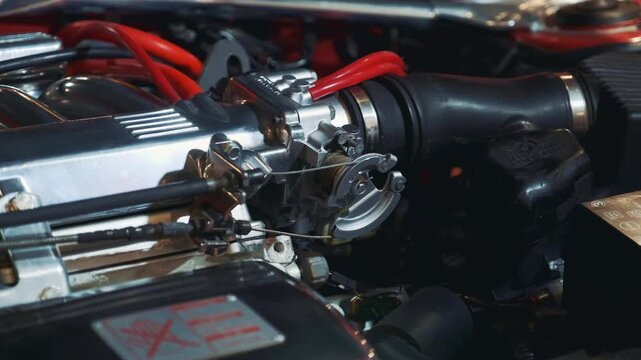 Detailed close-up of a speed control mechanism inside the engine compartment of a retro internal combustion vehicle, highlighting chrome linkages and red hoses.