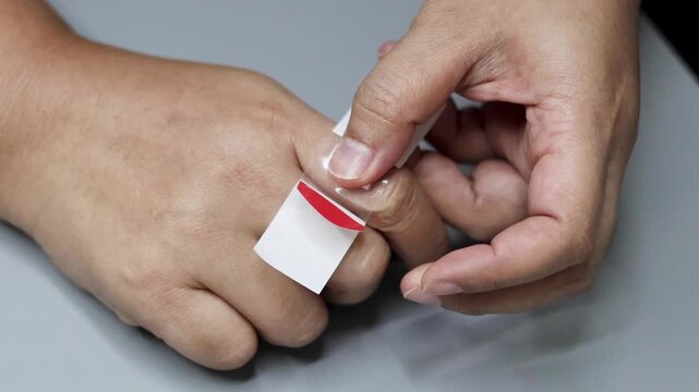 Woman hands applying transparent waterproof medical bandage on small finger wound for protection.