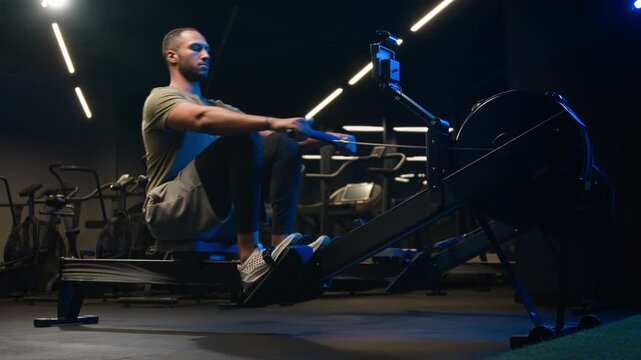 Sporty African American male man fitness trainer using rowing machine in gym sportsman endurance workout strong athlete pulling rope equipment training muscles for healthy lifestyle physical strength