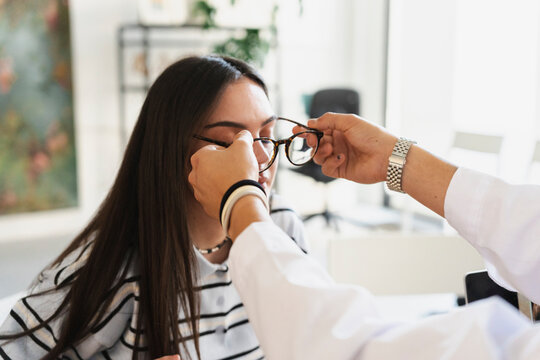 An optometrist carefully adjusts new glasses on a young female patient during an eye examination in a bright clinic. The doctor helps her test the frame fit.