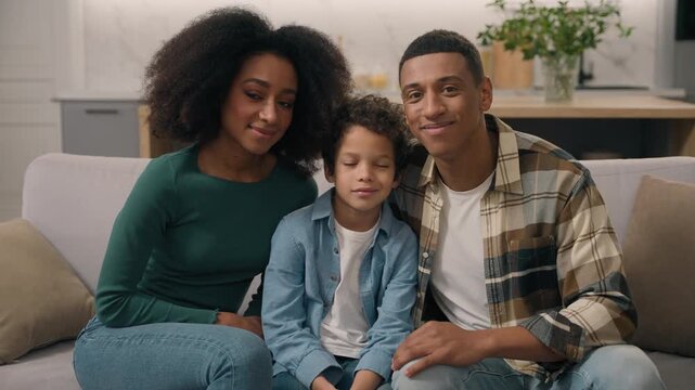 Cute happy African American family parents son sitting looking at camera at home loving ethnic portrait woman man caring mother father little boy child kid spouses homeowners posing together indoors