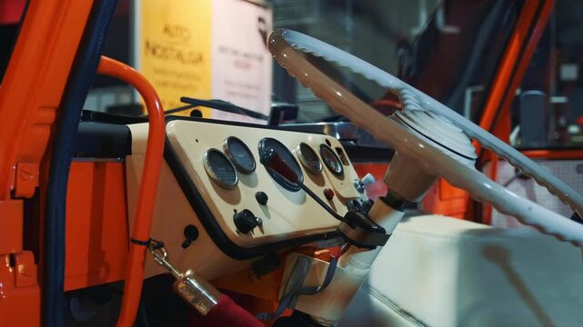 A close-up of a vintage car dashboard and cream-colored steering wheel inside a showroom featuring detailed gauges and orange structural elements. Classic retro style.