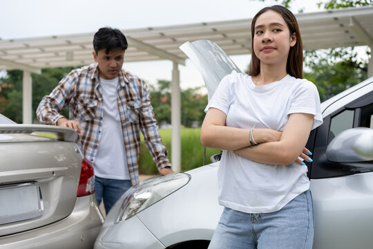 Asian drivers react to a possible car accident in a covered parking area, with a worried woman beside a vehicle and a man inspecting another car, illustrating insurance and roadside assistance.