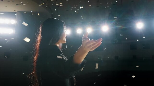 Female speaker celebrates a successful presentation on stage with a raised hand and falling confetti. Concept of victory, achievement, triumph and professional success.