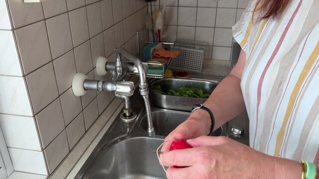 Close-up of a woman's hands taking fresh radishes one by one, cutting off the long thin roots and placing the prepared vegetables aside. Static shot.