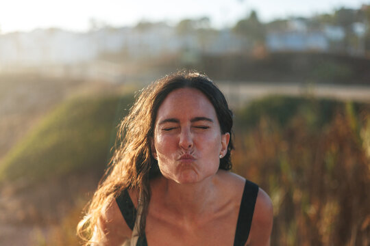 Woman puckering lips and closing eyes in playful expression during golden hour