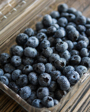 Fresh ripe blueberries with fine water droplets packaged in a clear plastic container on a wooden table.