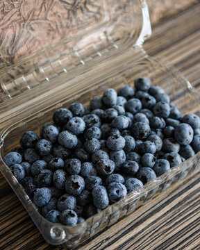 Fresh ripe blueberries with fine water droplets packaged in a clear plastic container on a wooden table.