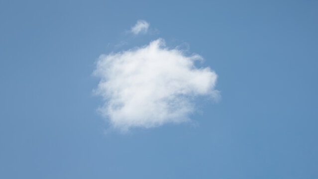 A single, fluffy white cumulus cloud drifts peacefully in the center of a vast, clear blue sky, the cloud has soft, wispy edges and a gentle texture, capturing a sense of calm and simplicity in nature