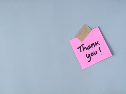 A pink adhesive note with the handwritten message thank you secured by brown adhesive tape on a clean grey background, perfect for business appreciation, customer service, and gratitude concepts