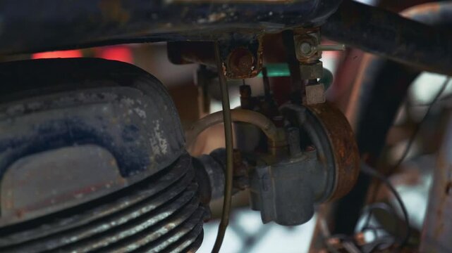 Detailed close-up showing rusty antique motorcycle engine parts with metal pipes and cables in an enclosed exhibition setting focused on mechanical textures.
