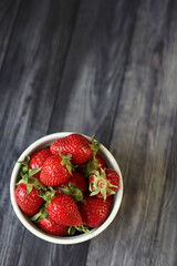 Fresh ripe strawberries in a white bowl on a dark rustic wooden background, viewed from above with copy space © ann197733