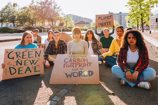 Group of young climate activists sitting on a city street with protest signs