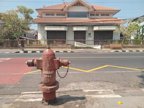 ​Red outdoor fire hydrant on a city street sidewalk with background of road and buildings on a sunny day. 

