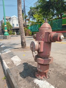 ​Red outdoor fire hydrant on a city street sidewalk with background of road and buildings on a sunny day. 

