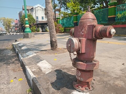 ​Red outdoor fire hydrant on a city street sidewalk with background of road and buildings on a sunny day. 

