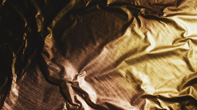 Close-up of crumpled gold foil with beautiful reflections and textured surfaces illuminated by warm light for artistic backgrounds