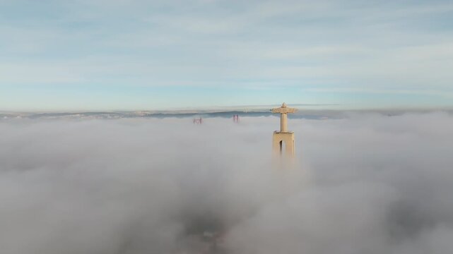 Slow panning drone of Cristo Rei, Lisbon at sunrise. Dense fog covers water. Christ the King and upper 25 de Abril Bridge visible. Portugal aerial