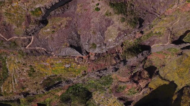 Drone video captures people hiking along the scenic, rugged PR1 trail between Pico do Areeiro and Pico Ruivo. Steep mountain slopes, dramatic rocky terrain, bright daylight, and vast vistas.
