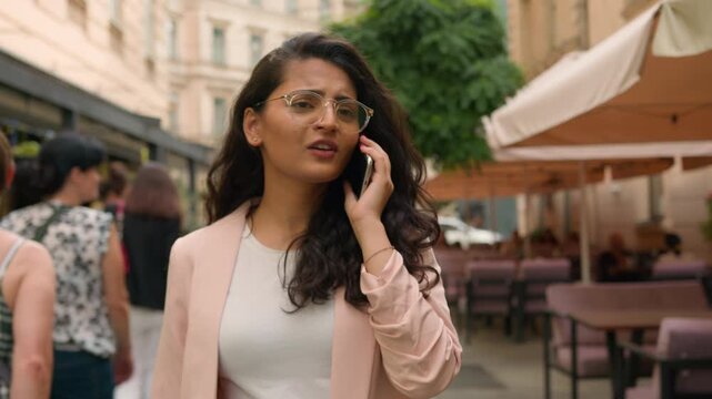 Happy smiling Indian woman talking on mobile phone walking in city street cafe Arabian ethnic female girl businesswoman student laughing call telephone discussion online connection travel outdoors