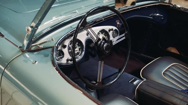 Close-up view of the steering wheel, dashboard, and bench seating inside a vintage sky blue American car, showcasing chrome details and dark upholstery in a well-lit interior.