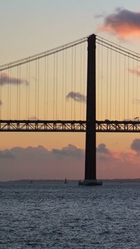 View of 25 de Abril Bridge famous tourist landmark of Lisbon connecting Lisboa and Almada on Setubal Peninsula over Tagus river on sunset. Lisbon, Portugal. Camera pan