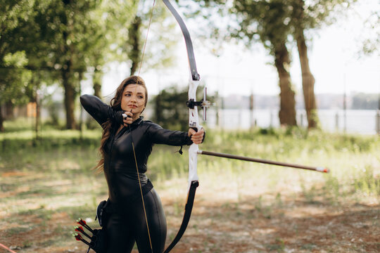 Woman practicing archery, drawing bowstring, aiming with concentration