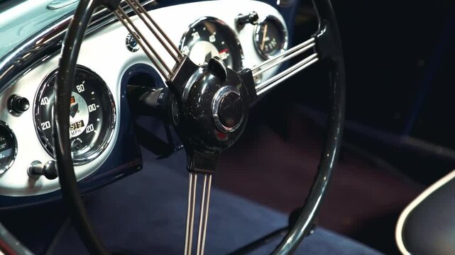 Close-up of a vintage vehicle's black multi-spoke steering wheel and chrome instrument panel with gauges inside the classic car interior.