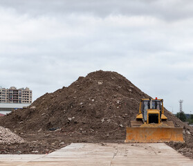 Heavy industrial yellow crawler bulldozer working at a construction site. Powerful earthmoving machinery vehicle clearing ground near a huge pile of soil dirt and stones under an overcast sky.  © Dmitry Presnyakov