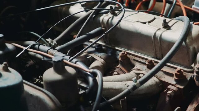 Detailed close-up of a rusty vintage car engine with cast metal parts, hoses, and pipes inside the engine bay of a classic automobile, showcasing aged mechanical components.