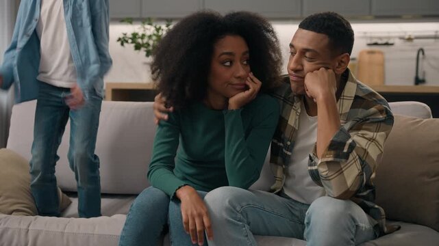 Stressed African American parents sitting couch with noisy little boy child son having tantrum in living room tired mom dad irritated by active kid jumping sofa unhappy female male pair indoors house