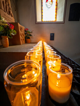 Glowing votive candles inside a church with stained glass window